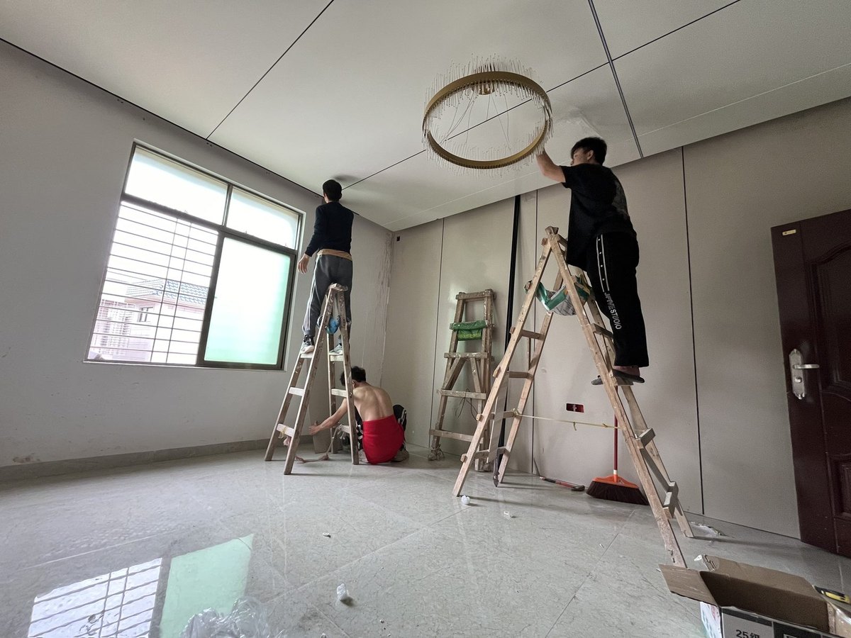 湛江工装装修工程实拍，圆环吊灯安装现场，两把梯子各站一人、下面一人递工具，爱果儿装饰